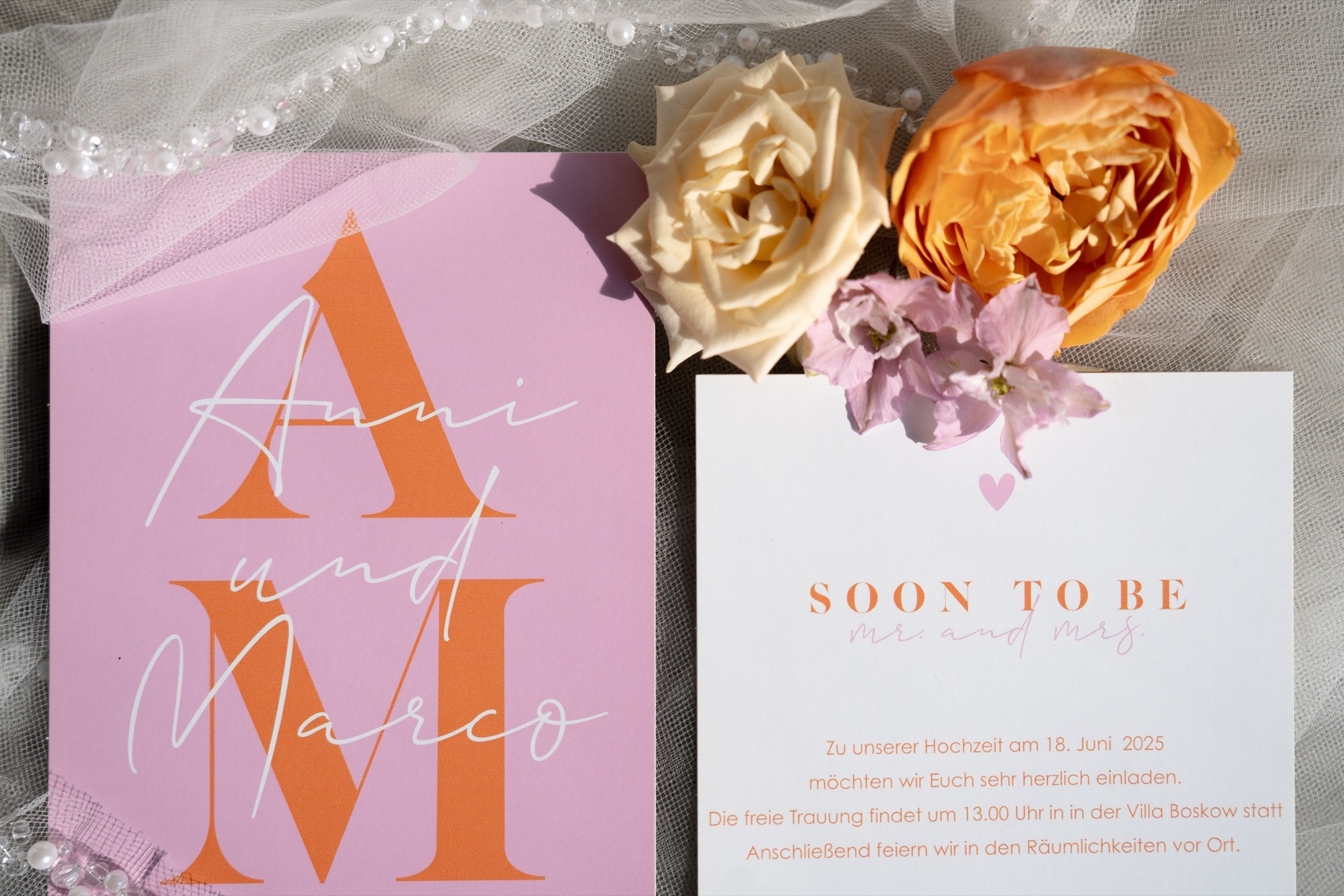 Hochzeitseinladung mit großen Initialen neben Rosen auf einem Brautschleier