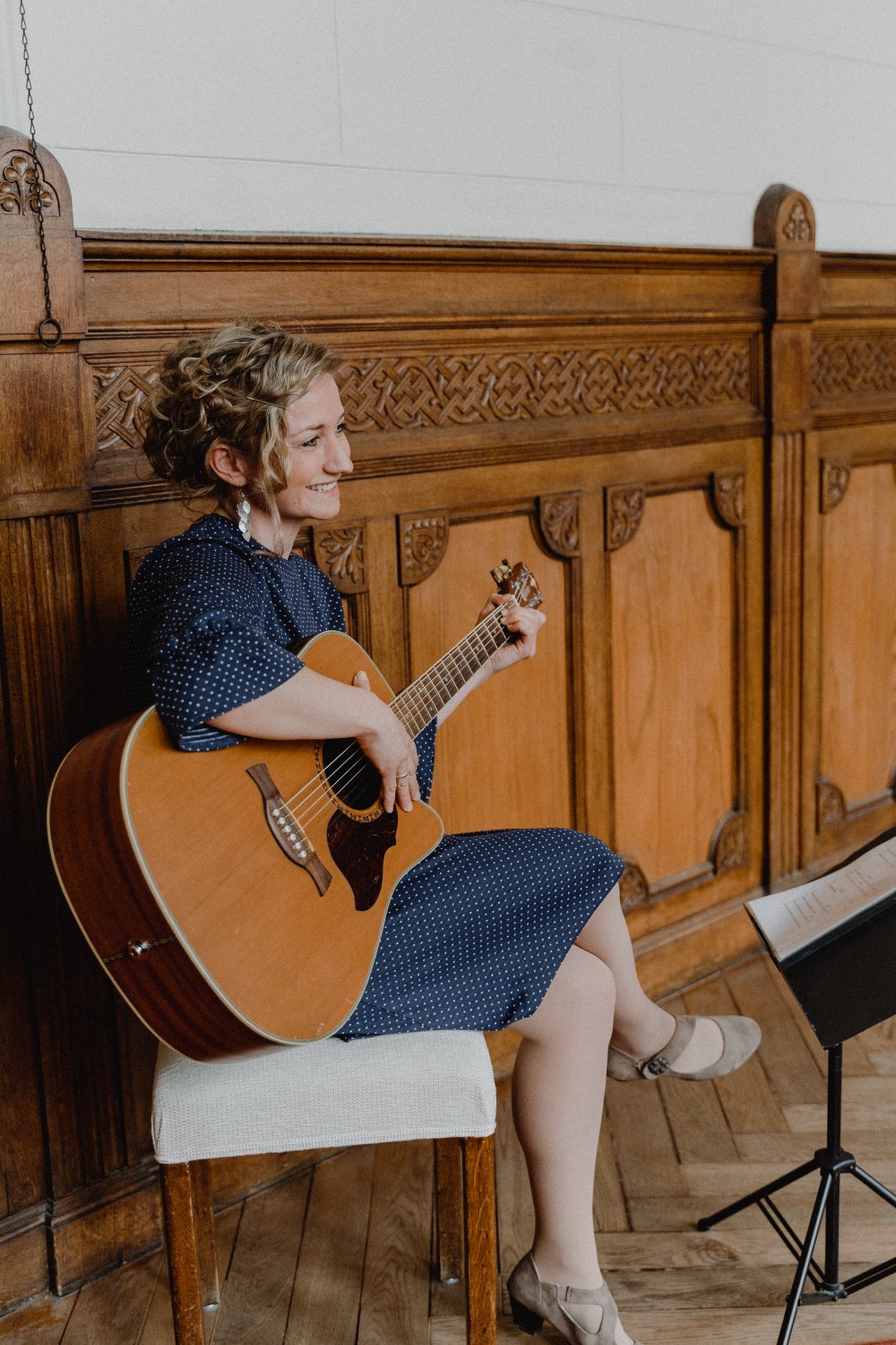 Anne Fraune sitzt lächelnd mit Gitarre vor einer geschnitzten Holzvertäfelung
