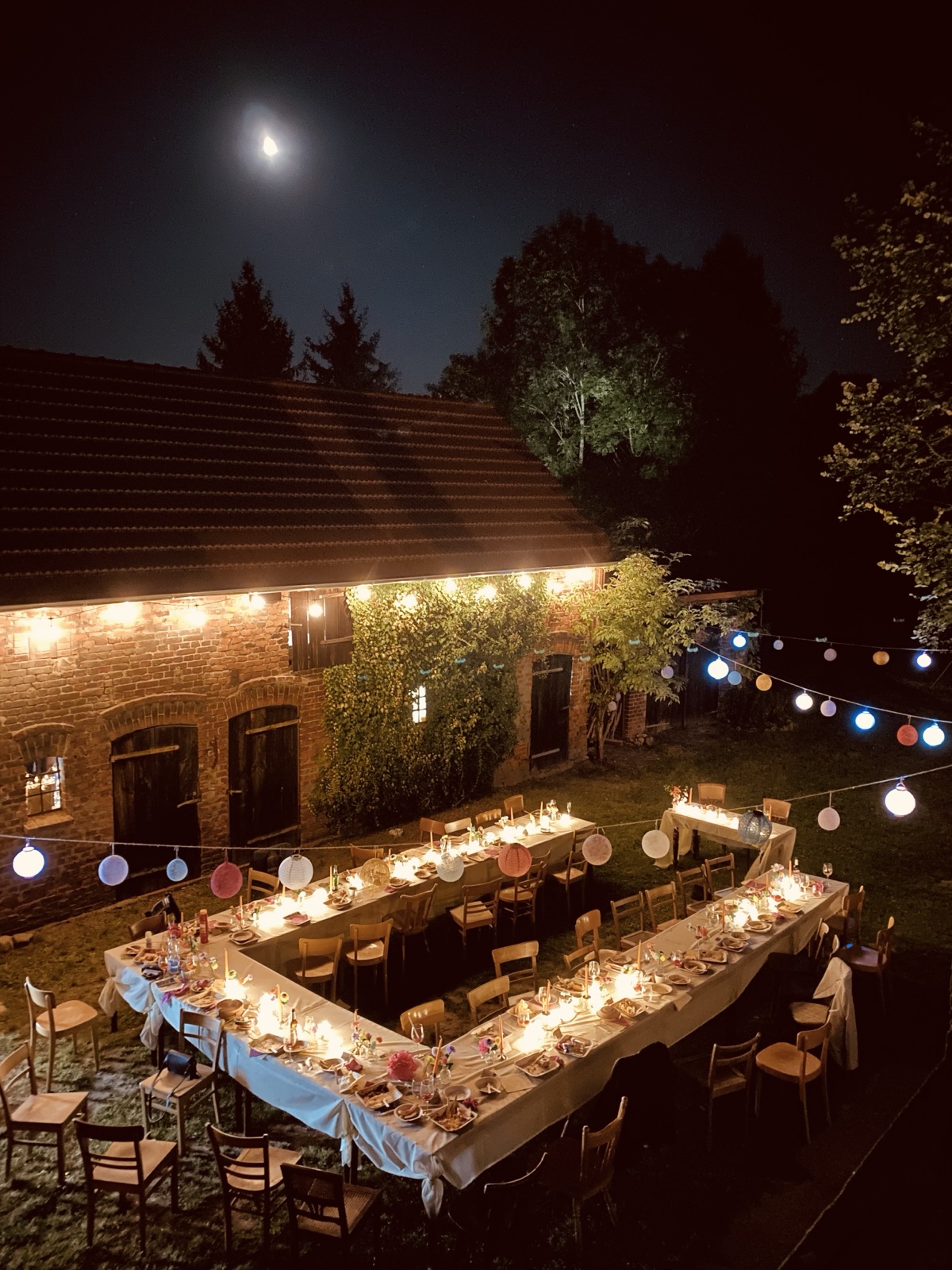 Gedeckte Tafeln bei Nacht im Hof vor der Scheune, mit Lichterketten und Lampions